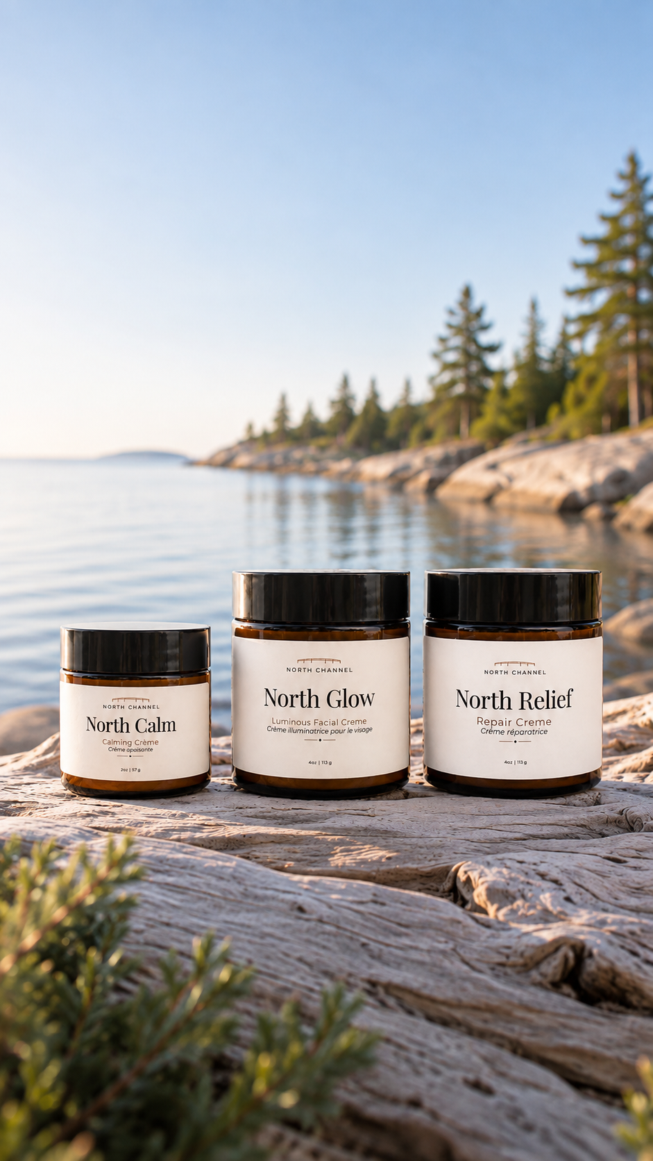 North Calm, North Glow, and North Relief crèmes standing on sun-bleached rock, still water and a pine shoreline behind them