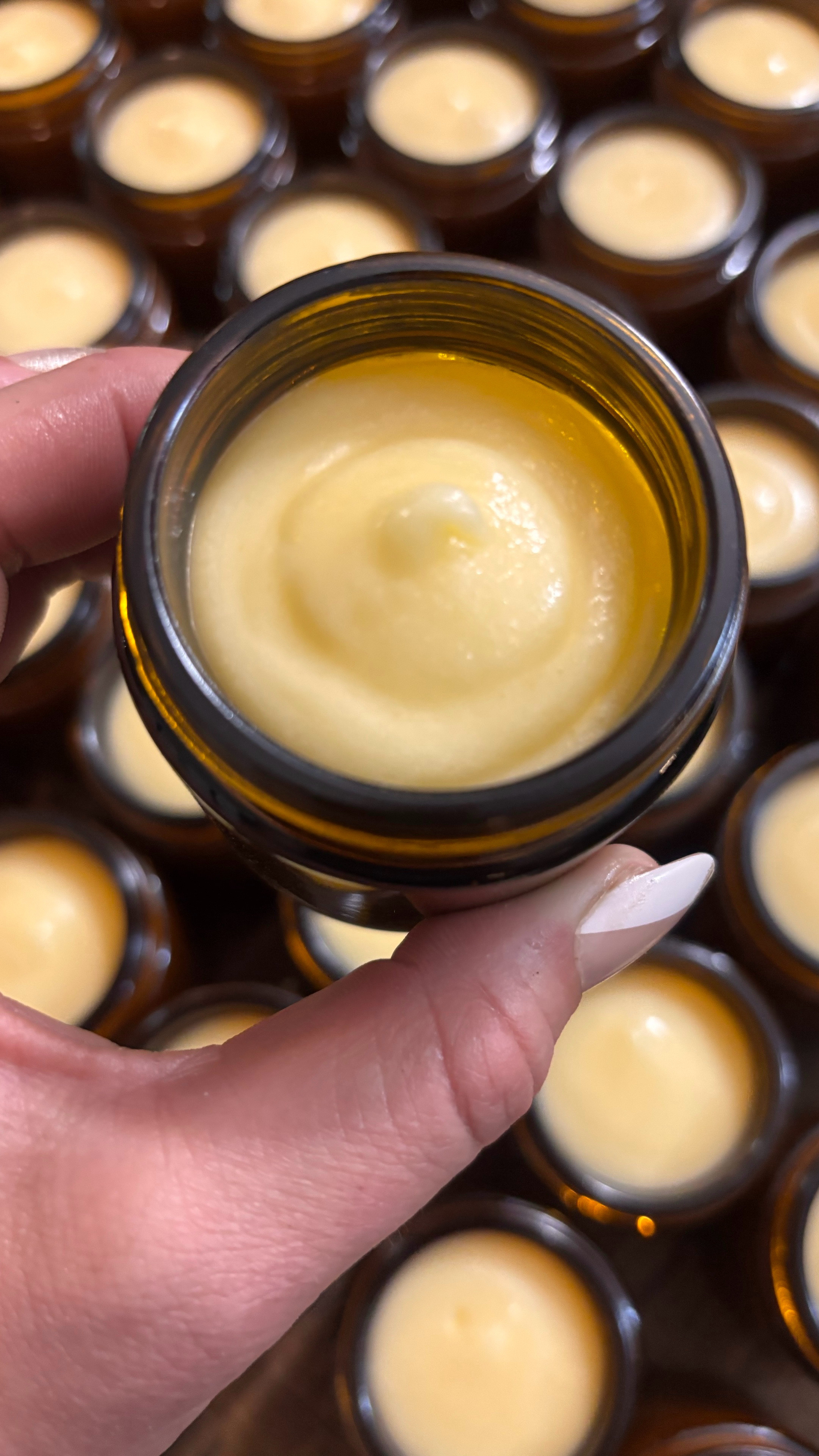 An open jar of North Channel's tallow crème held by hand, with a fresh small batch behind