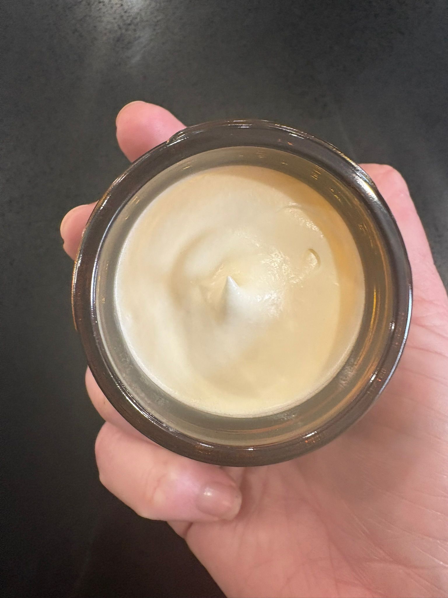A freshly filled jar of tallow crème, held by hand
